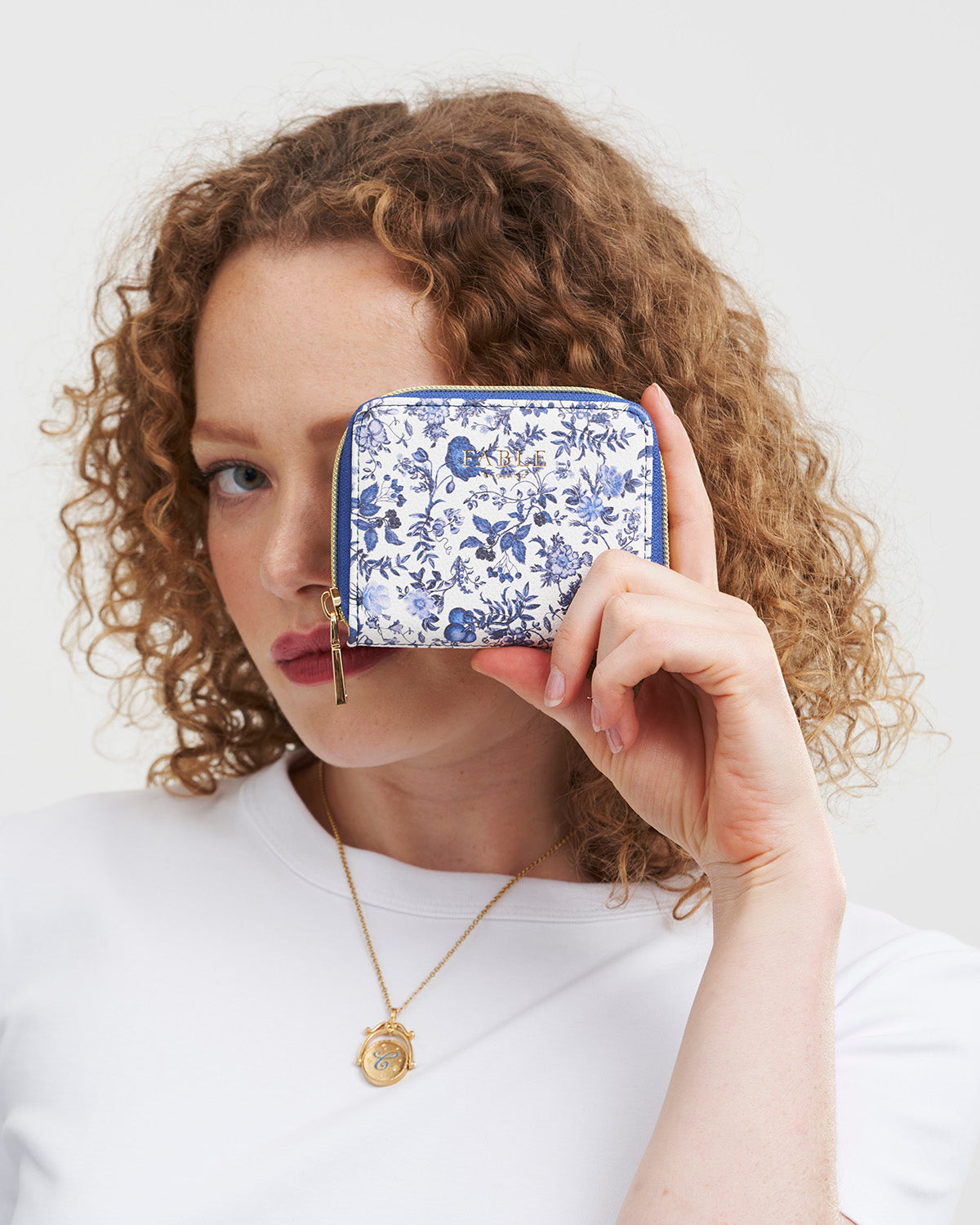 Woman holding a blue floral wallet in front of her face against a white background