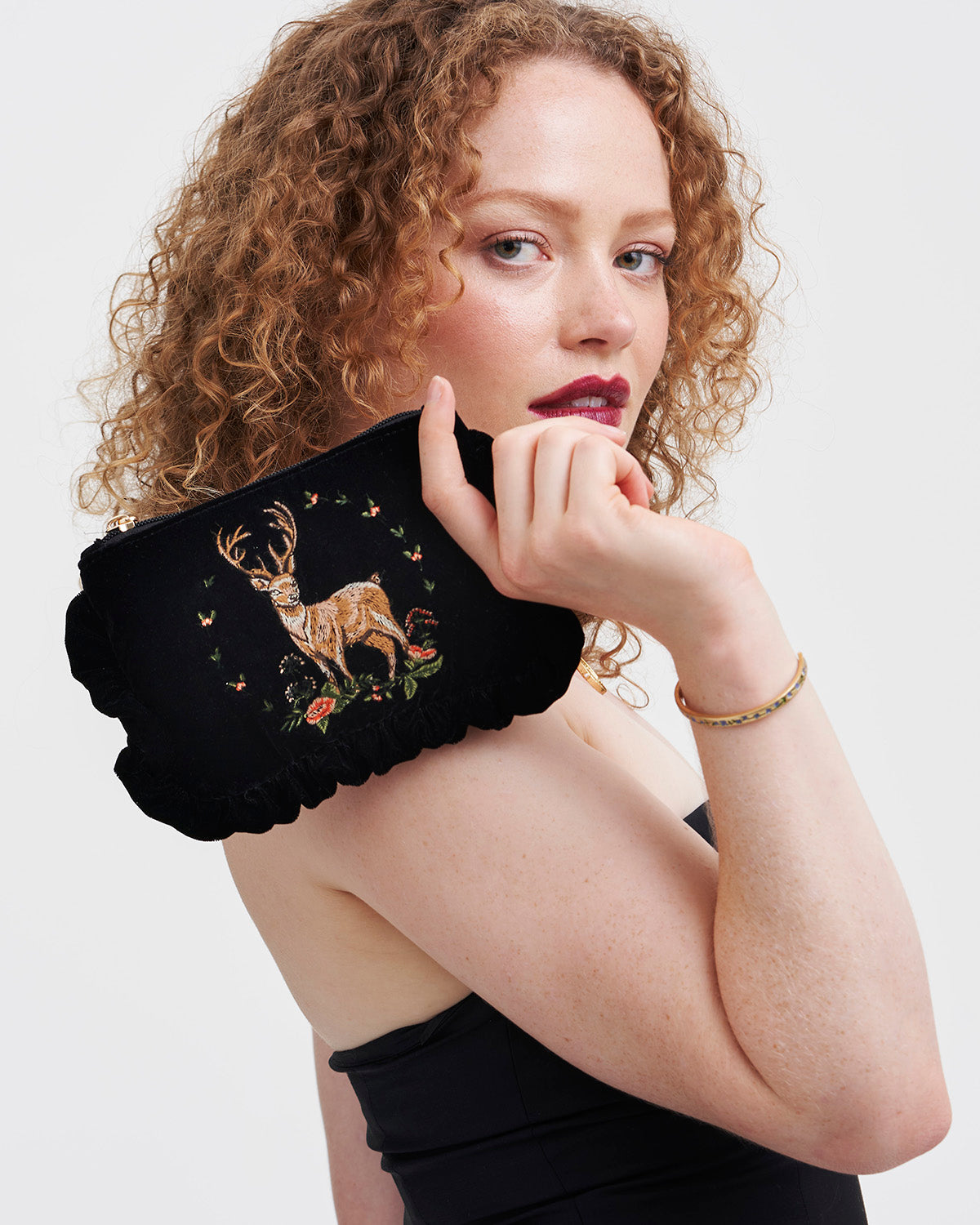 Woman holding a black clutch with deer embroidery against a white background