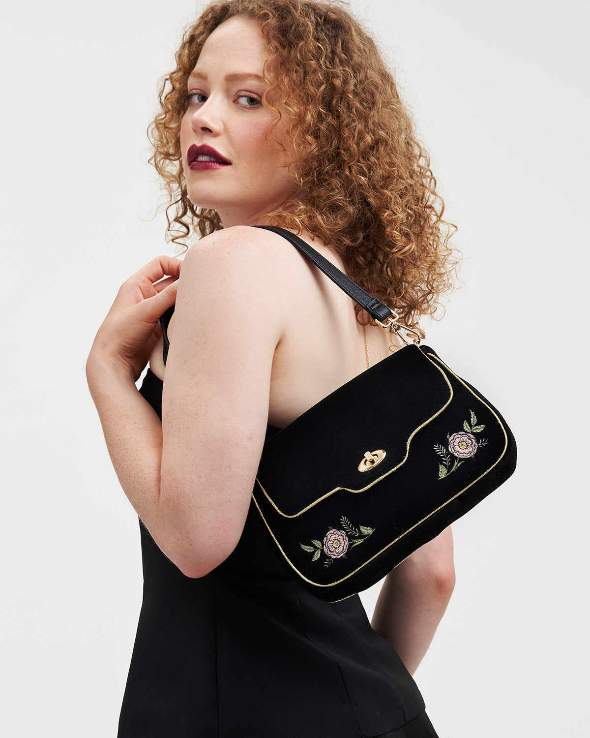 Woman holding a black handbag with floral embroidery on a white background
