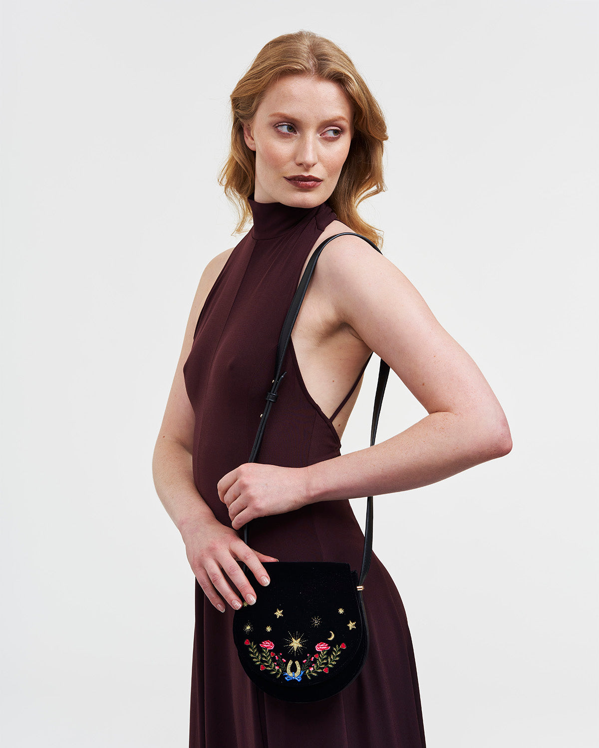 Woman holding a black handbag with floral embroidery against a plain background