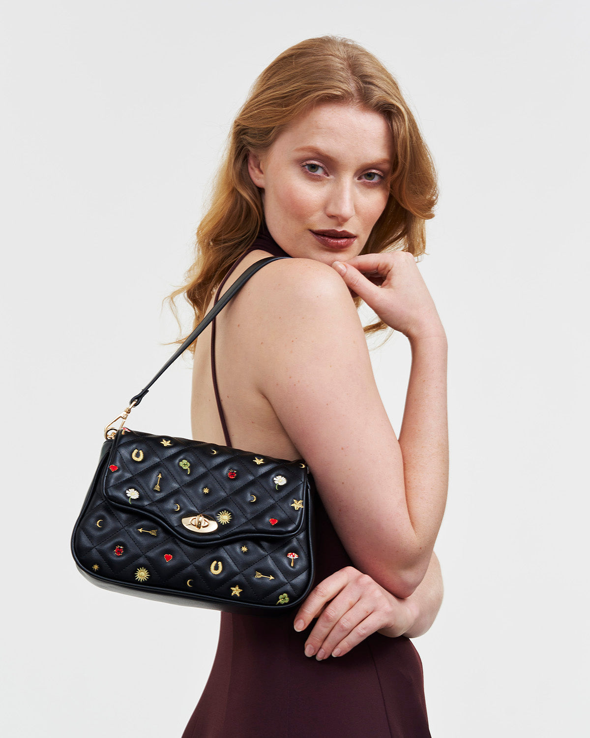 Woman holding a black quilted handbag with celestial embroidered motifs on a white background