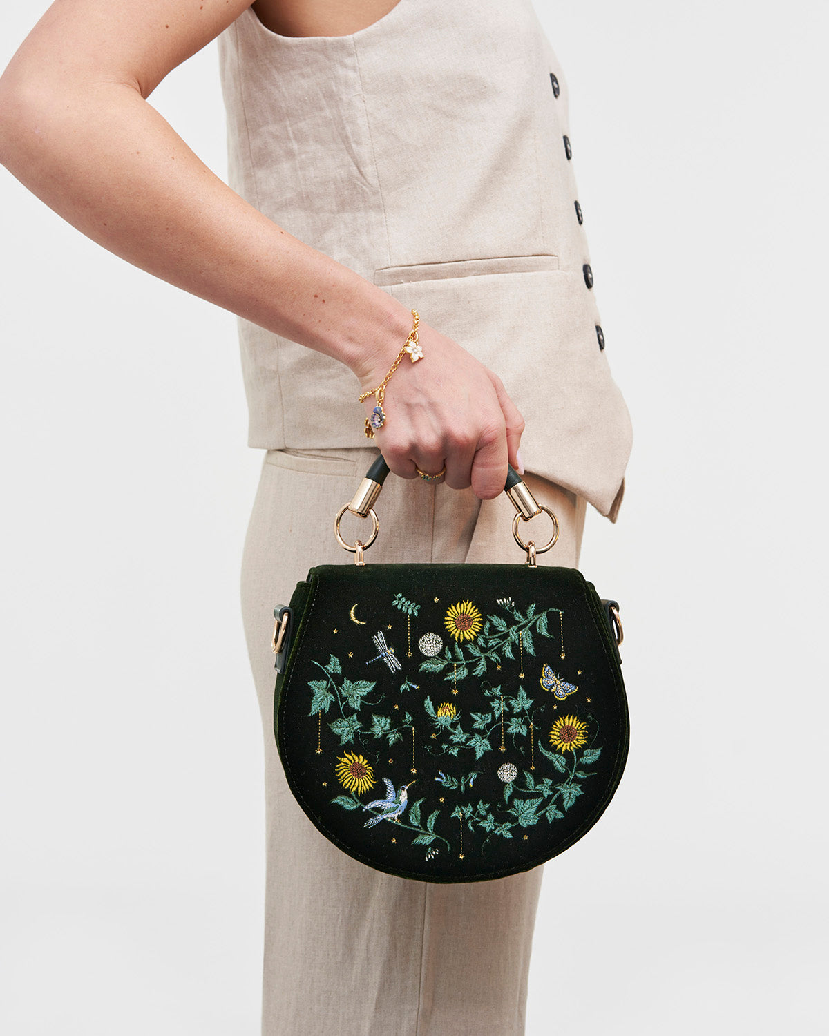 Person holding a green handbag with floral embroidery against a plain background