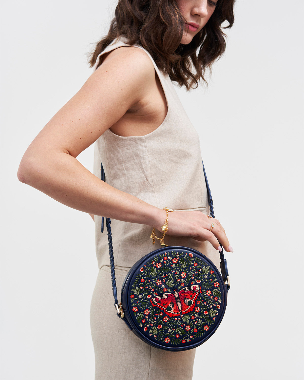 Woman holding a round embroidered bag with floral and butterfly design on a plain background