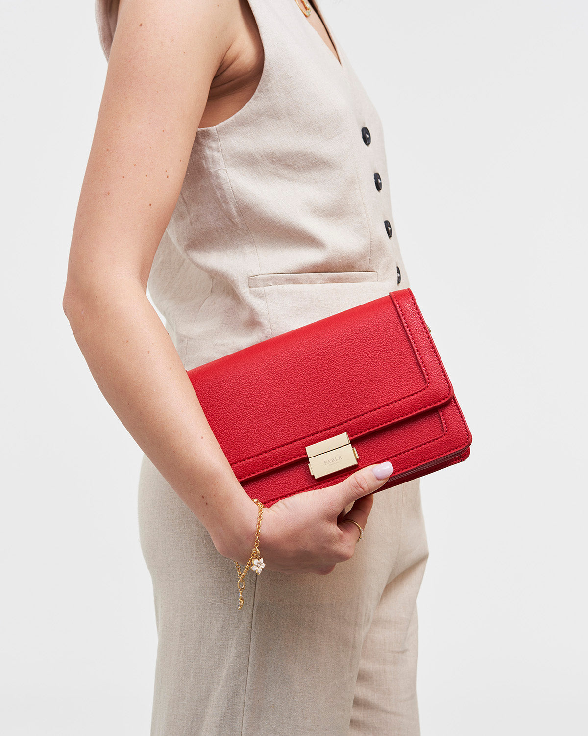 Red clutch held by a person wearing a beige outfit on a white background