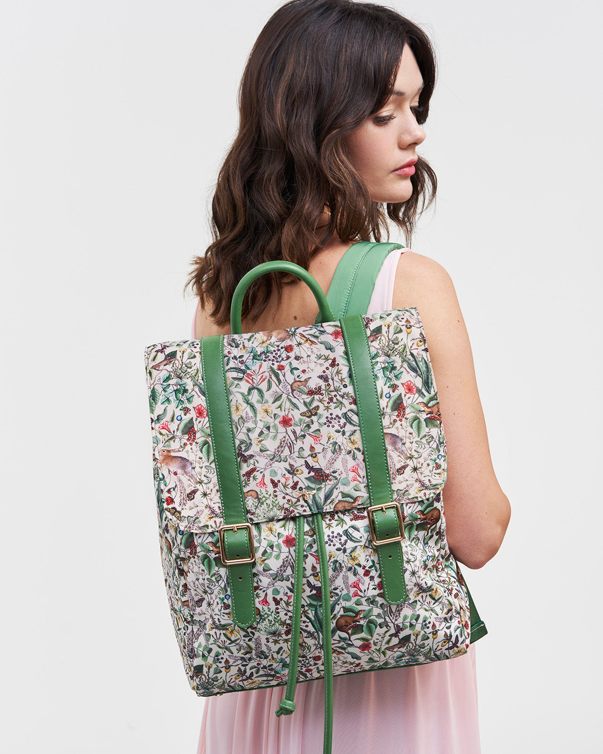 Woman wearing a floral backpack with green straps on a white background