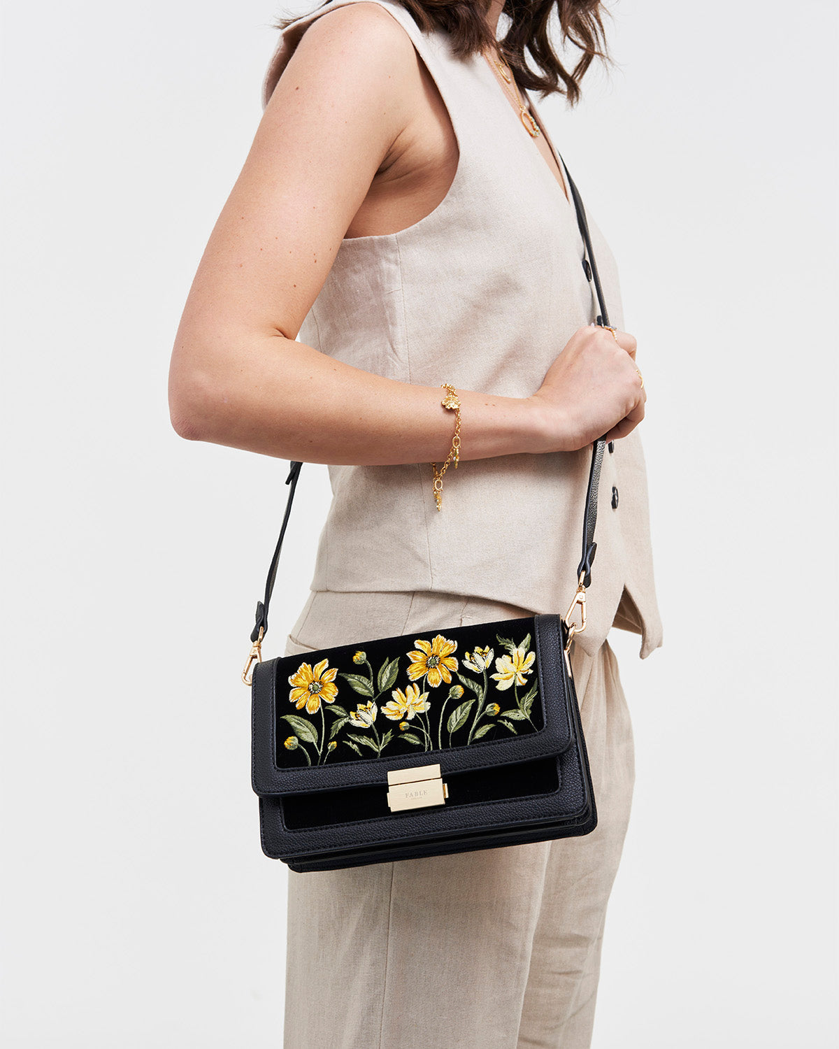 Person holding a black handbag with floral design on a plain background