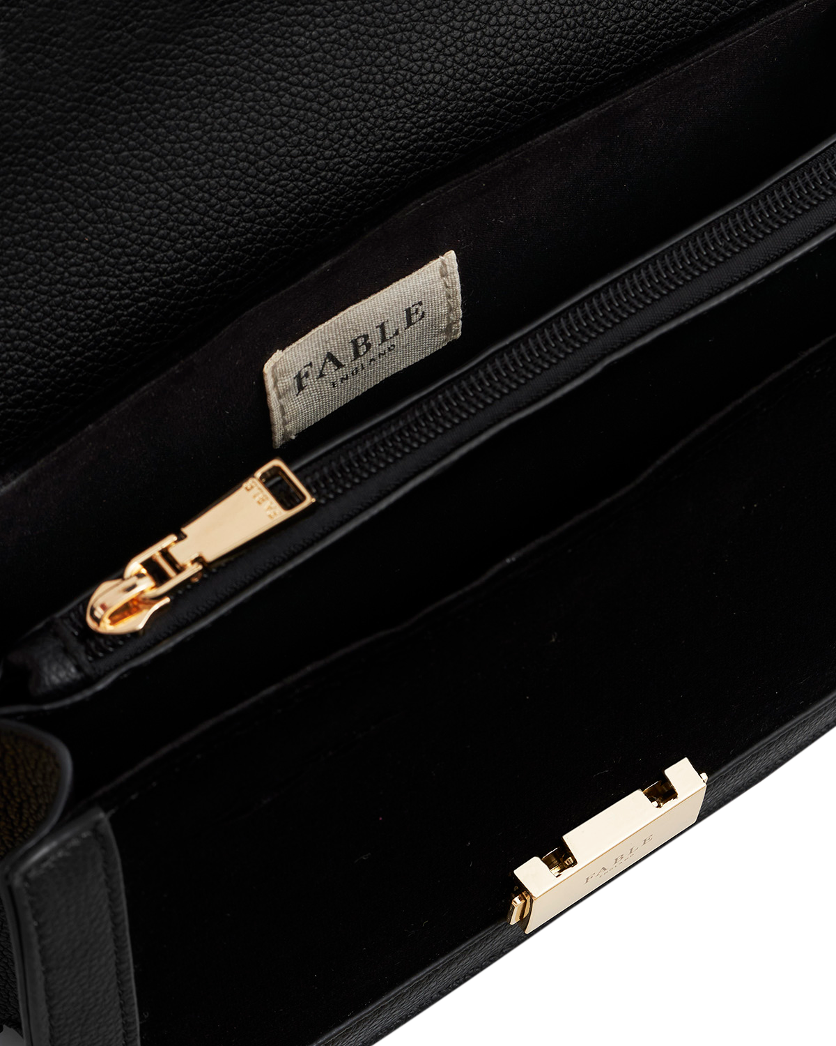 Black leather clutch with gold zipper and 'Fable' brand label.