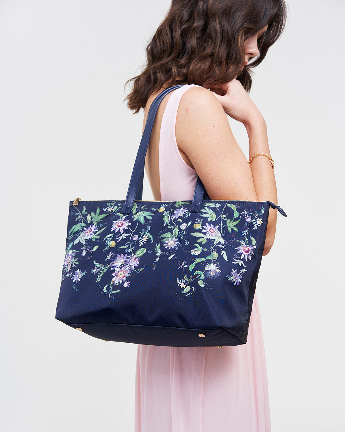 Woman holding a navy tote bag with floral pattern against a plain background