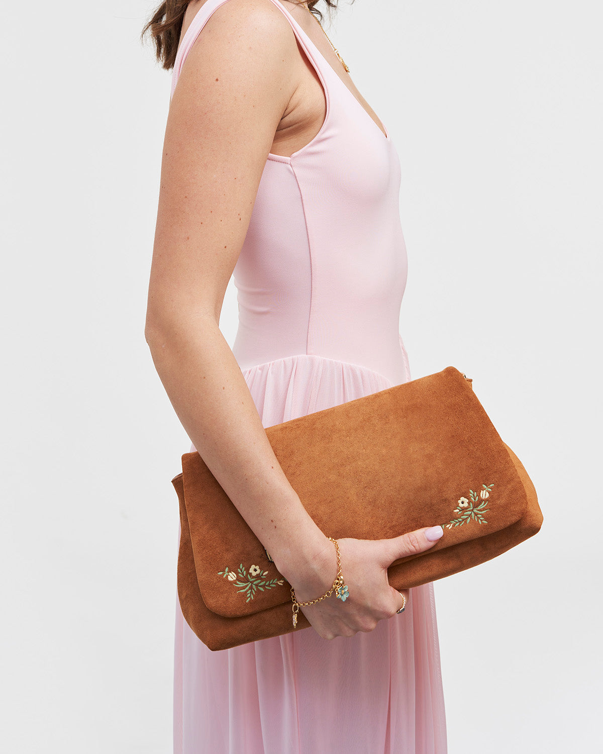 Person holding a brown suede clutch with floral embroidery against a white background
