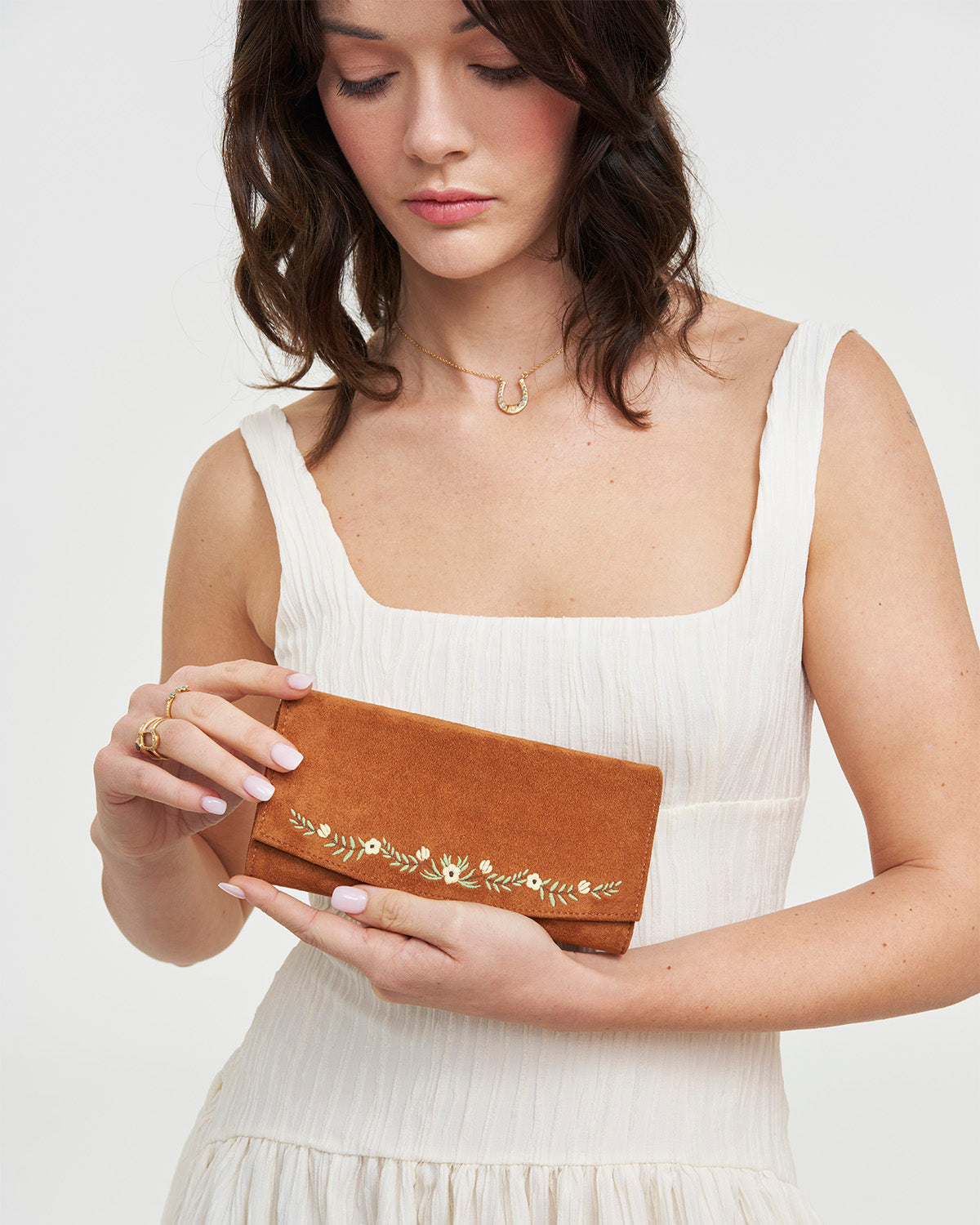 Woman holding a brown wallet with floral embroidery against a white background