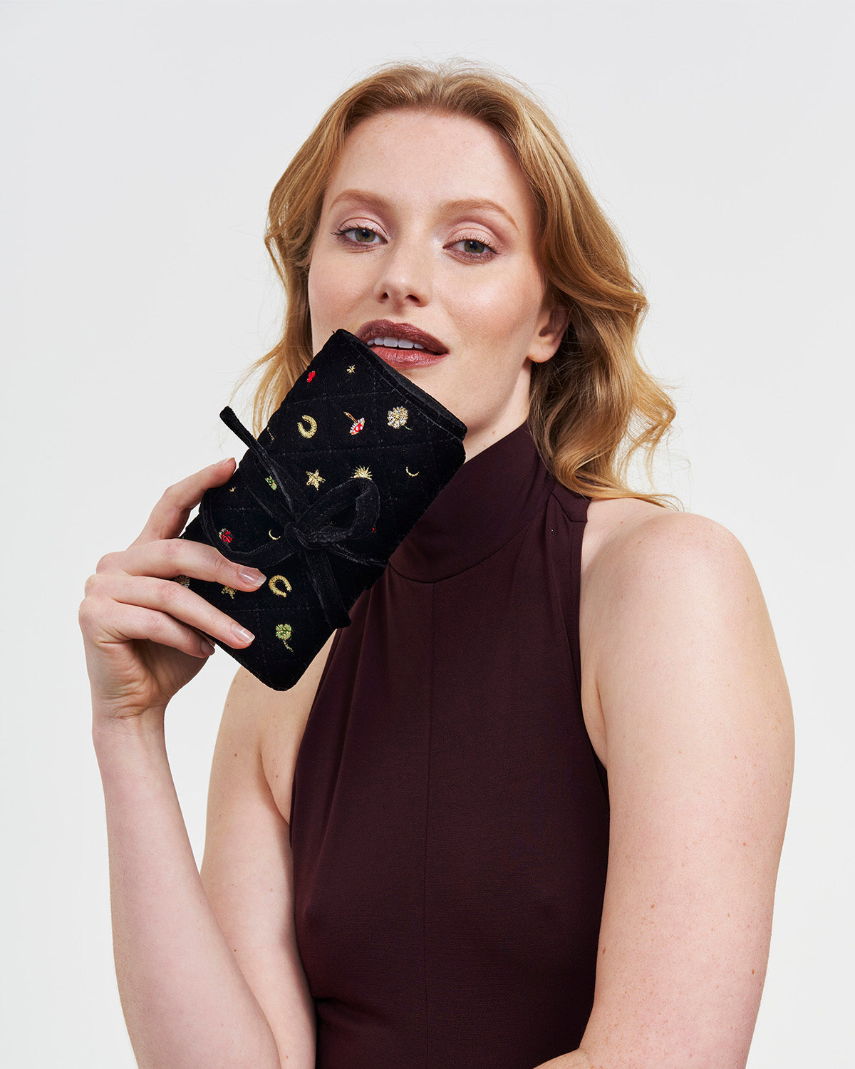 Woman holding a black embroidered jewellery roll against a plain background