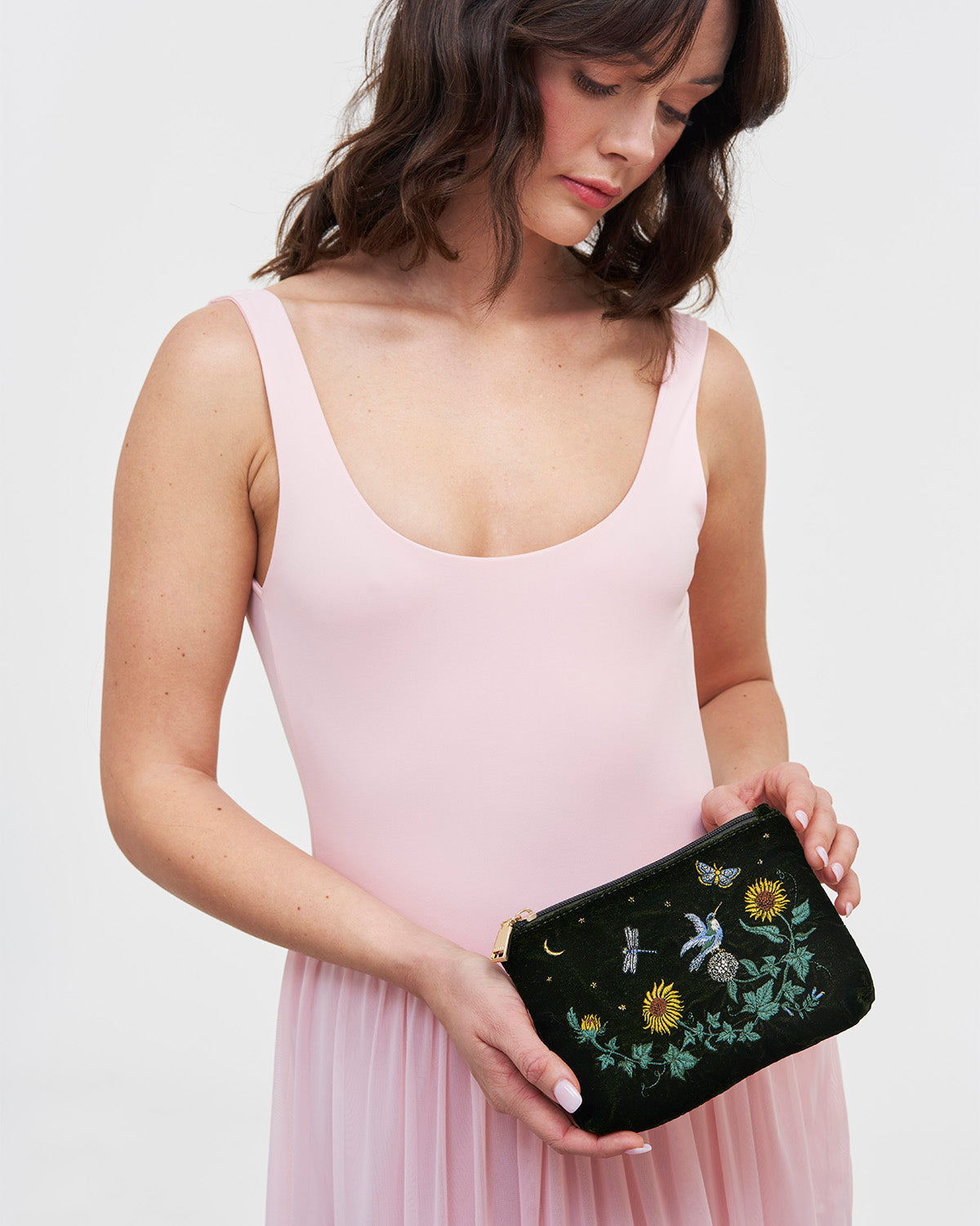 Woman holding a green clutch with floral embroidery against a plain background
