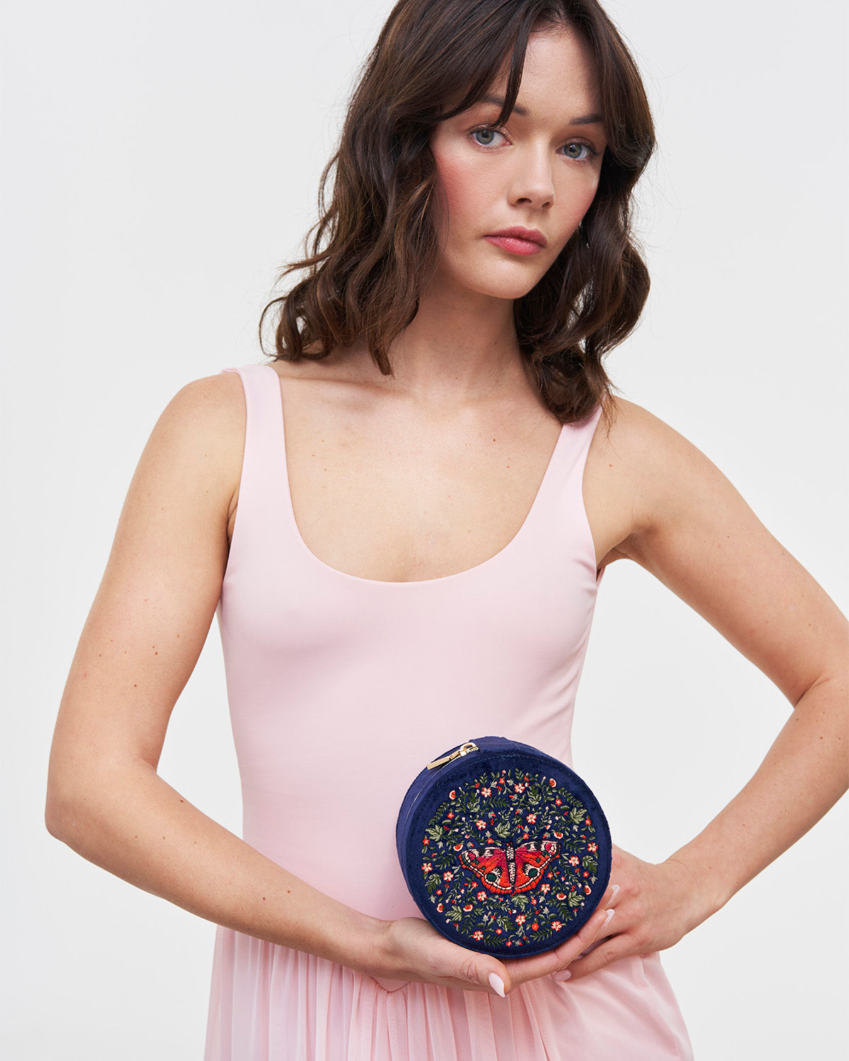 Woman holding a round, embroidered jewellery box against a plain background