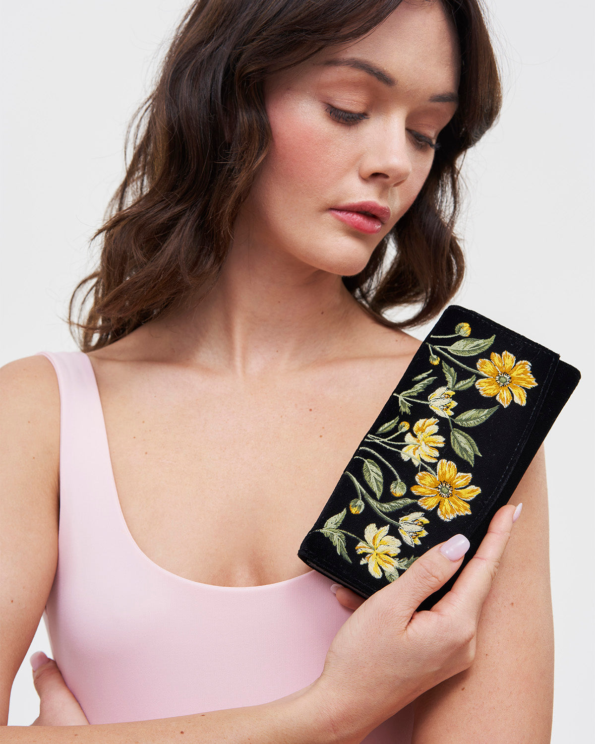 Woman holding a black clutch with yellow floral embroidery against a white background