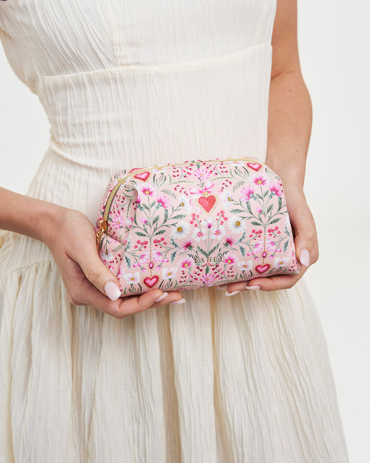 Floral clutch held by a person wearing a white dress on a light background