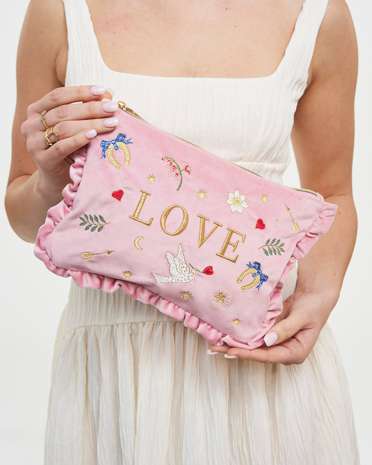 Person holding a pink pouch with 'LOVE' embroidery against a white background