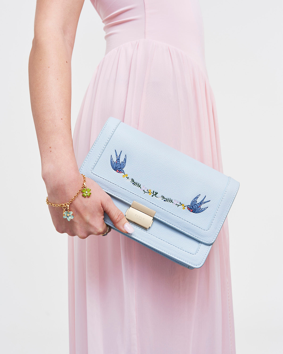 Light blue clutch bag with floral embroidery held by a person wearing a pink dress.