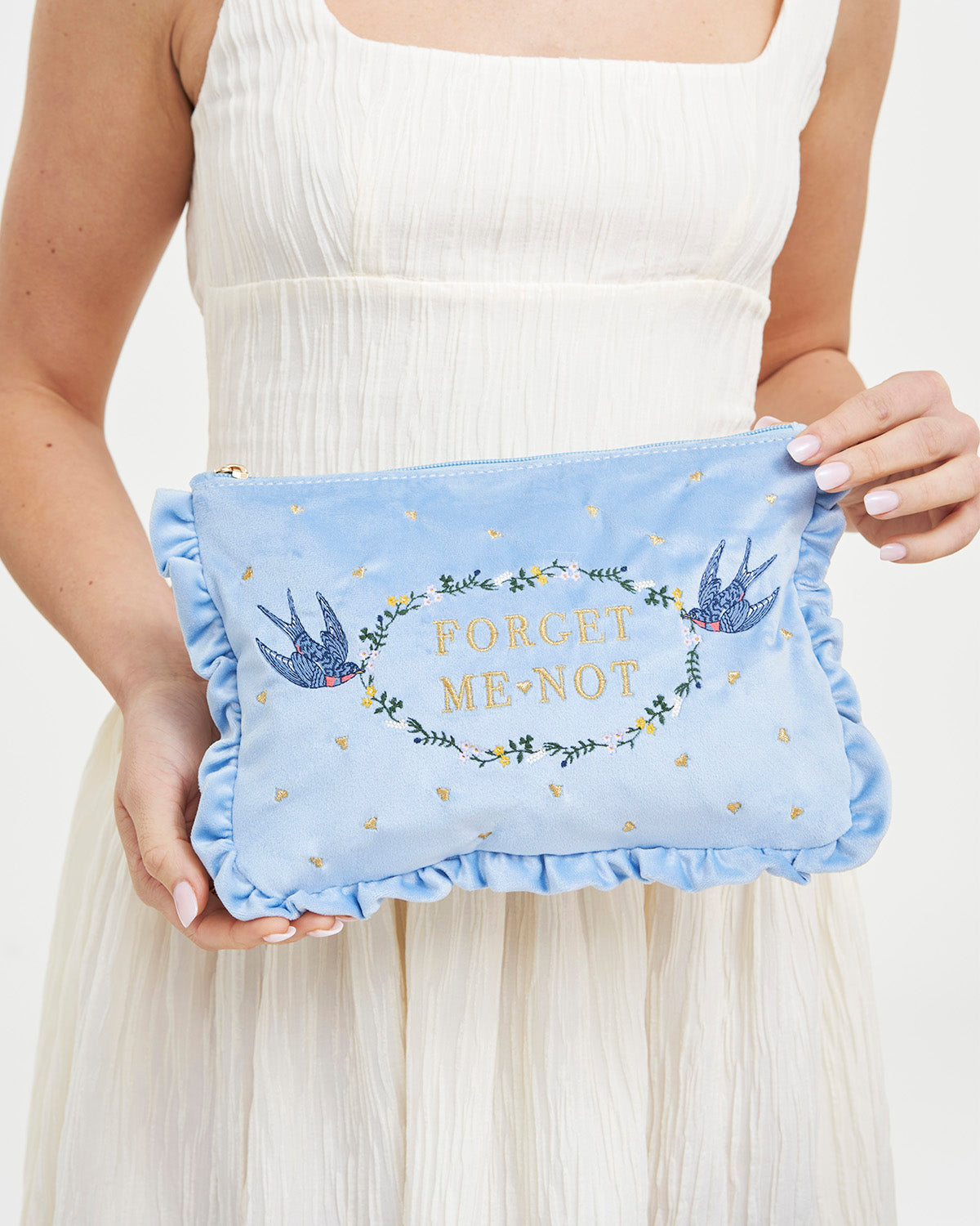 A person holding the Blue Forget Me Not Velvet Embroidered Pouch featuring blue birds and floral design.