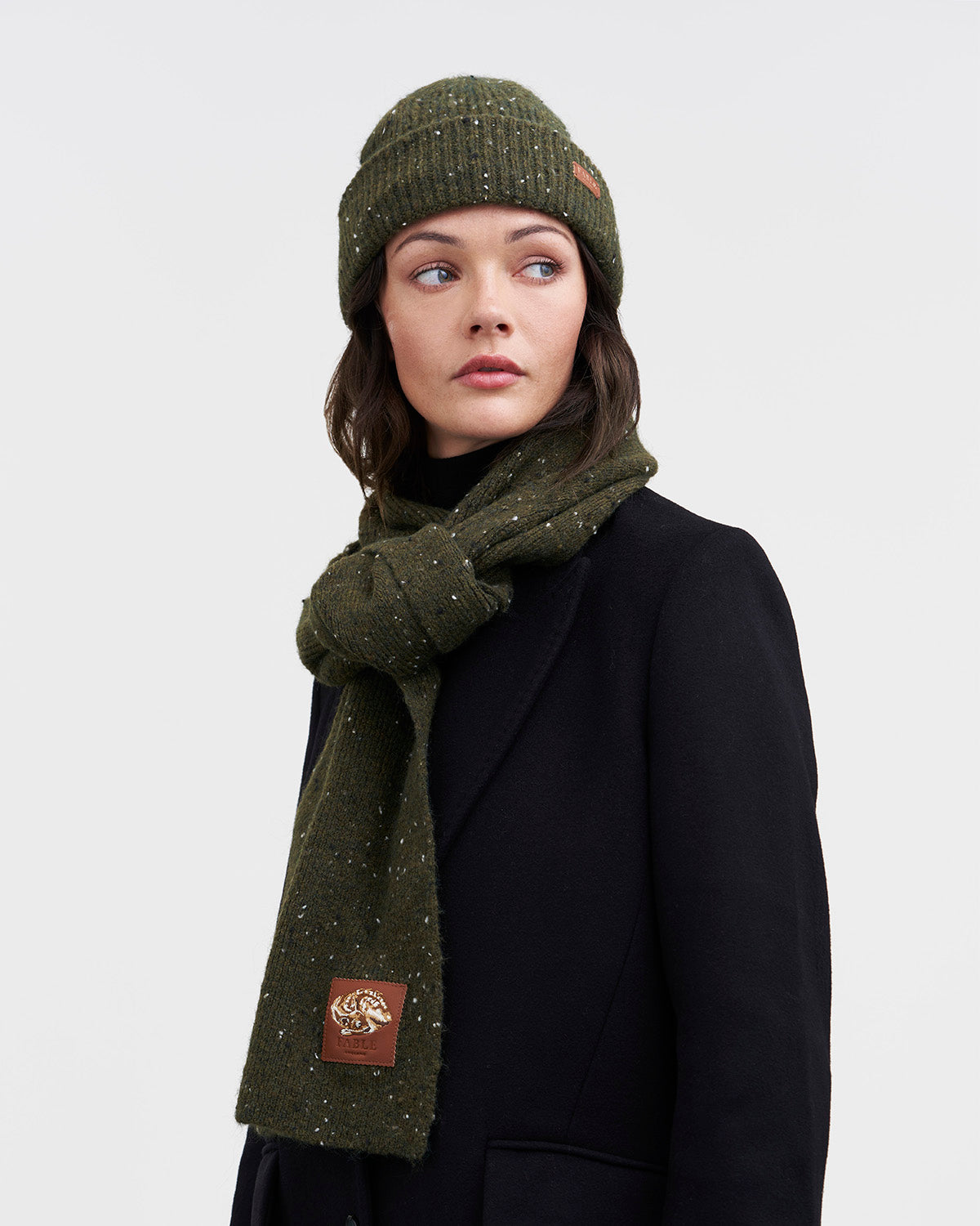 person wearing matching green knitted scarf and hat on white background