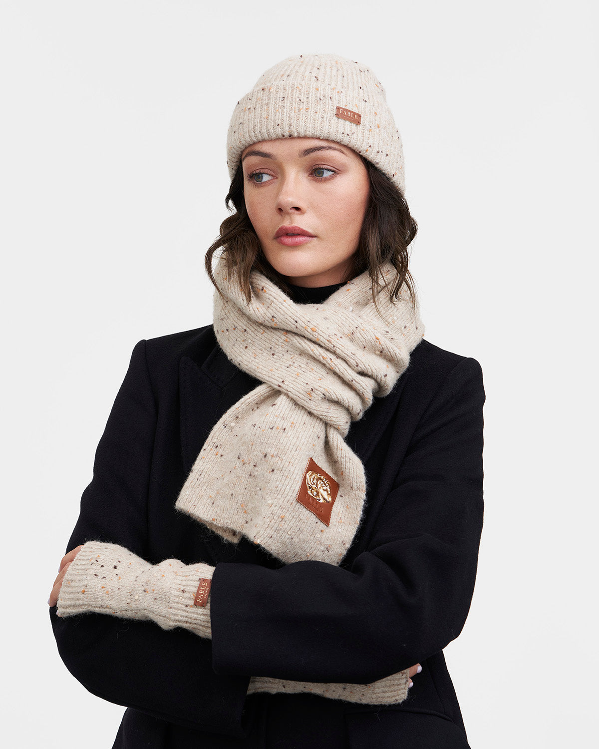 Person wearing a tupe knit hat, scarf, and gloves with a brand logo on a white background