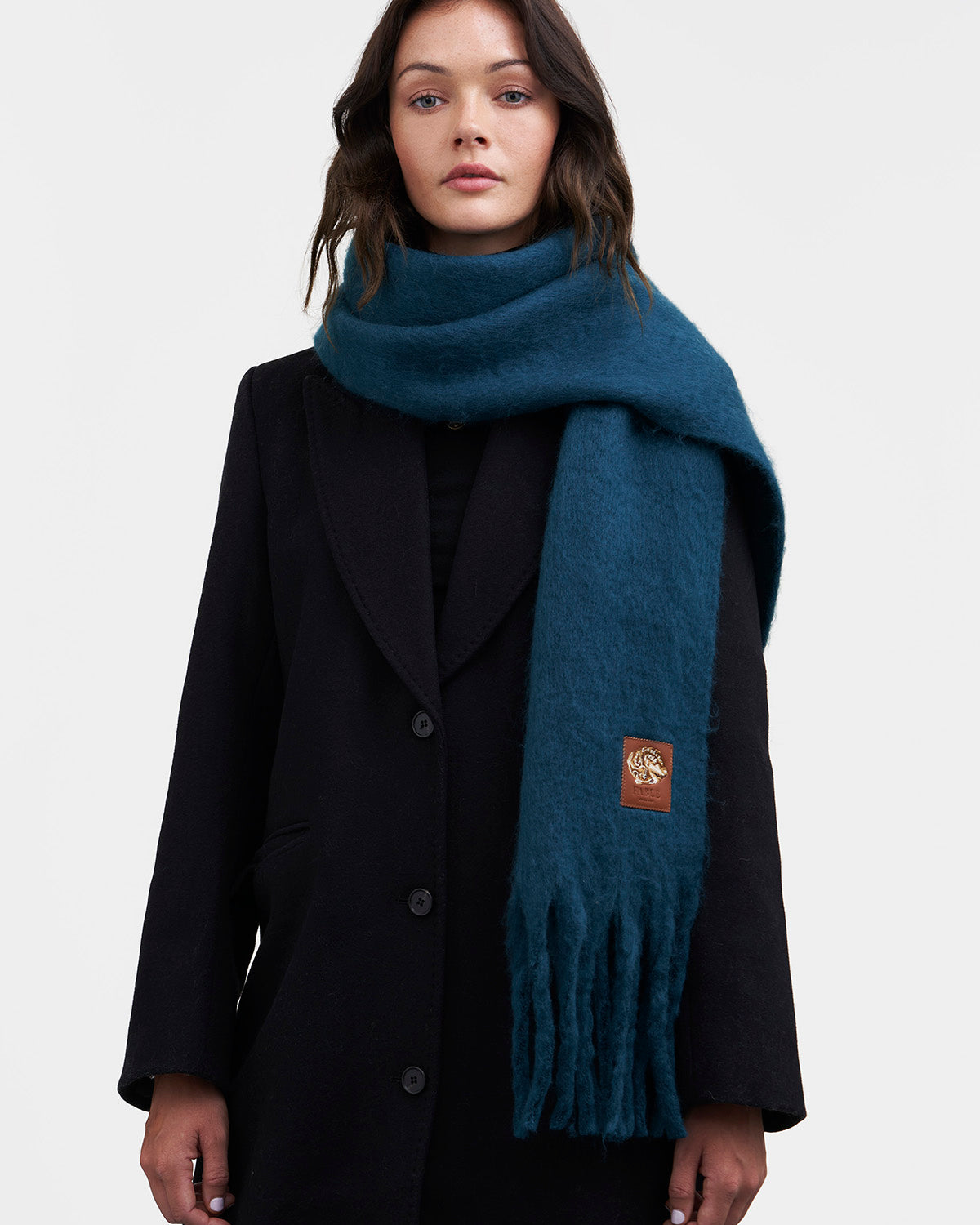 Woman wearing a dark coat and teal scarf with a brand logo on a white background