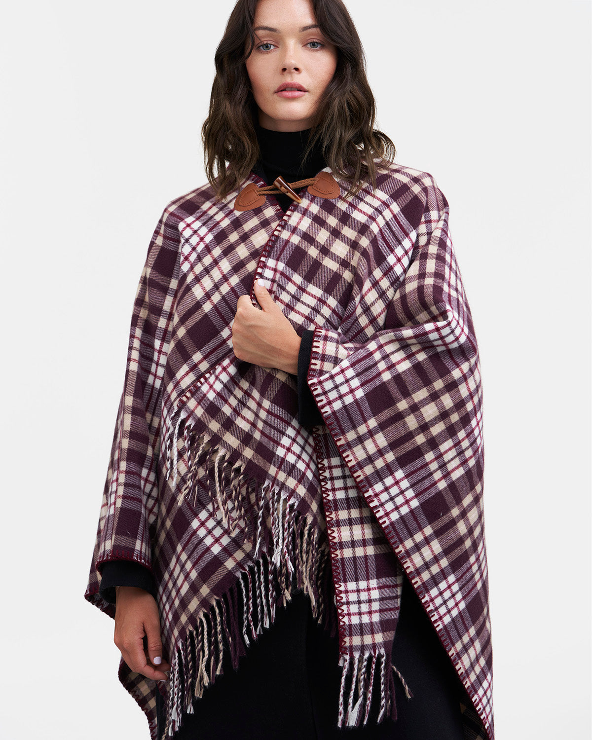 Woman wearing a red and white checkered cape with fringes on a white background