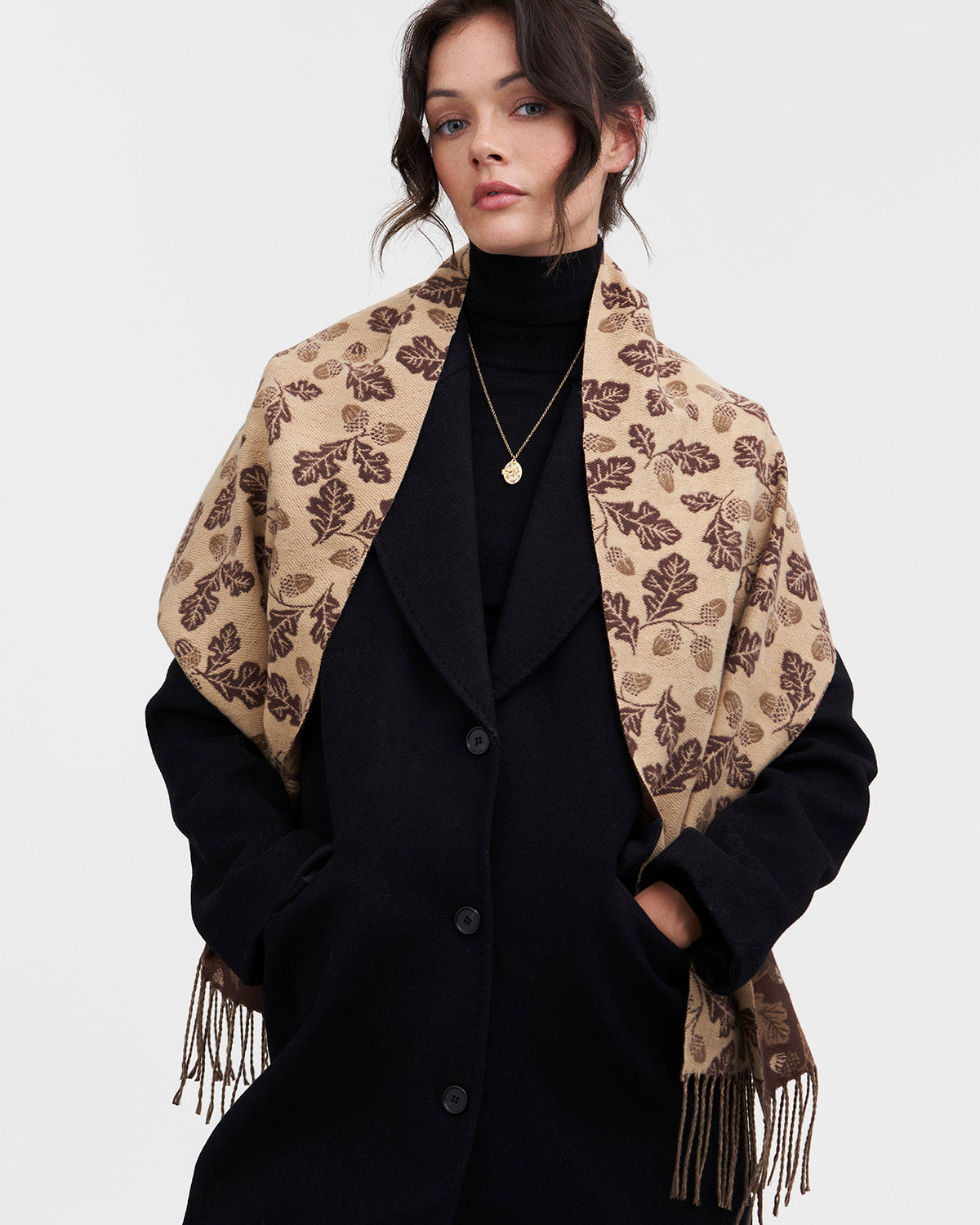 Woman wearing a black coat and beige patterned scarf on a white background