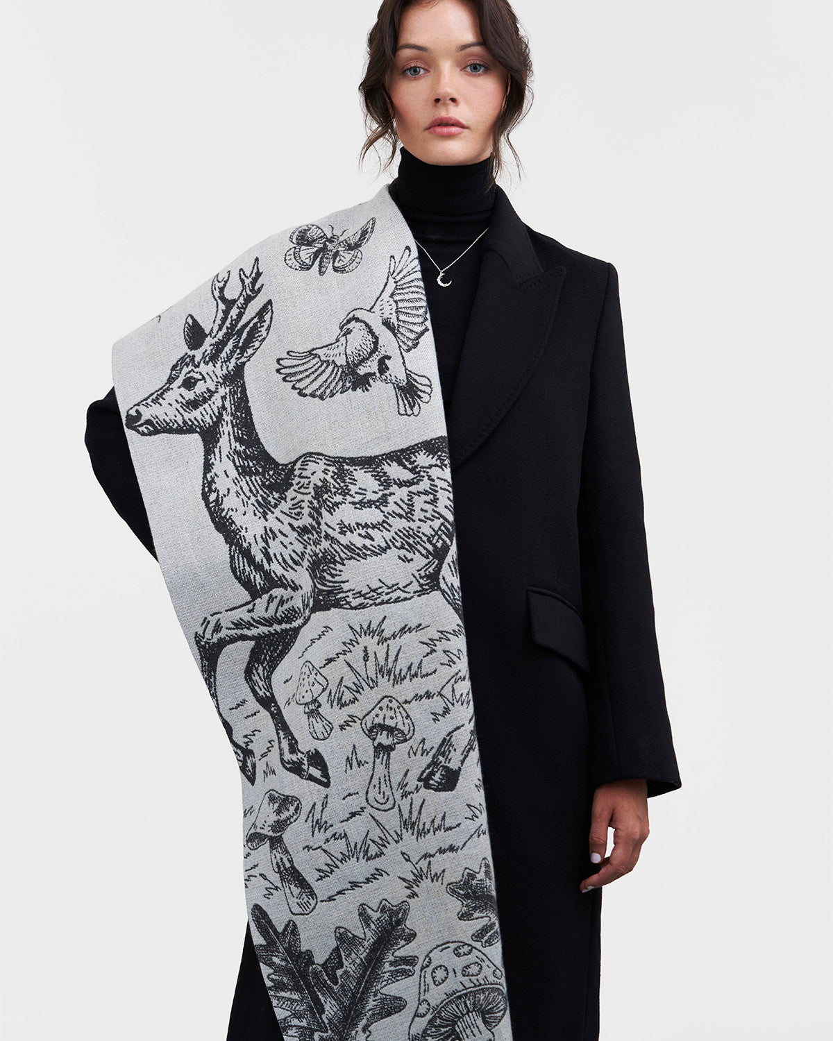 Person wearing a black coat with a large, patterned scarf featuring deer and bird designs.
