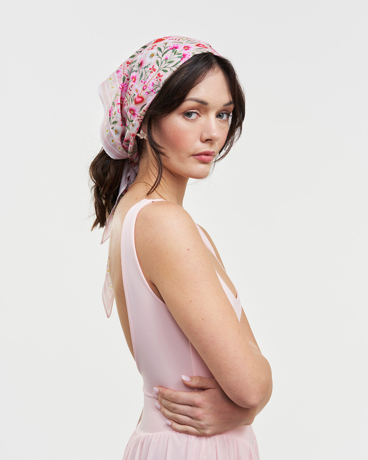 Woman wearing a floral headscarf and pink dress against a white background