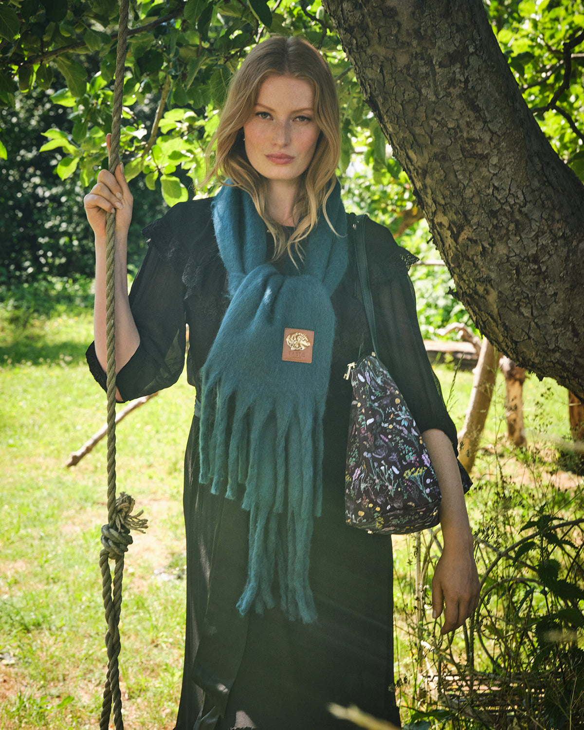 Woman wearing a teal boucle scarf and holding a patterned bag in a natural setting