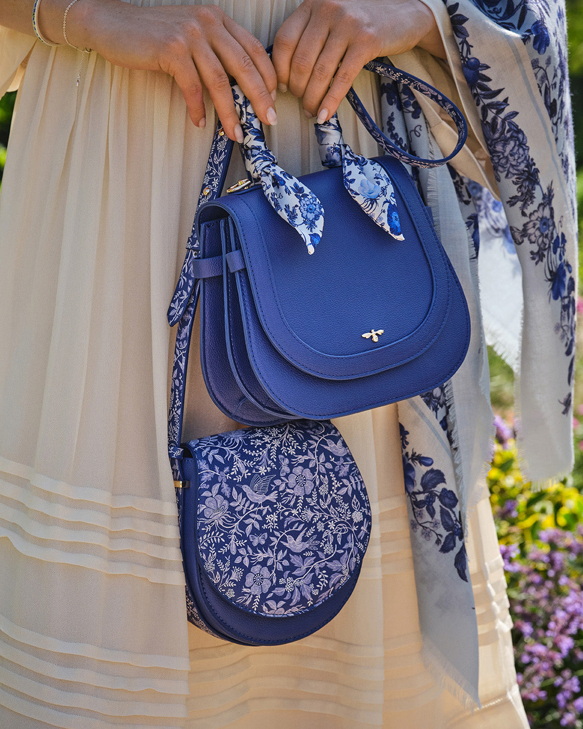 Blue handbag with floral strap held by a person wearing a beige dress with floral patterns.