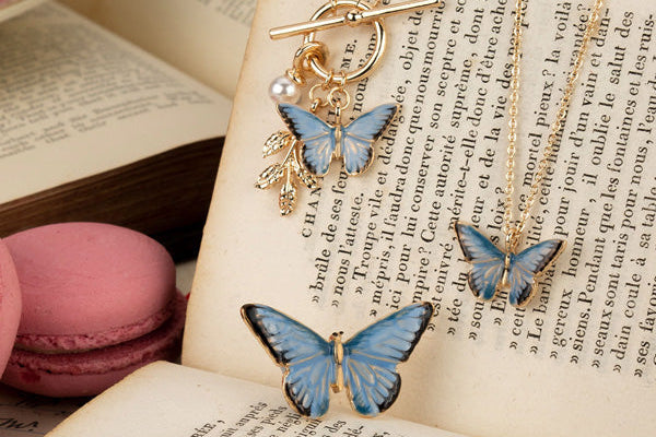 Butterfly-themed jewelry set on an open book with pink macarons.