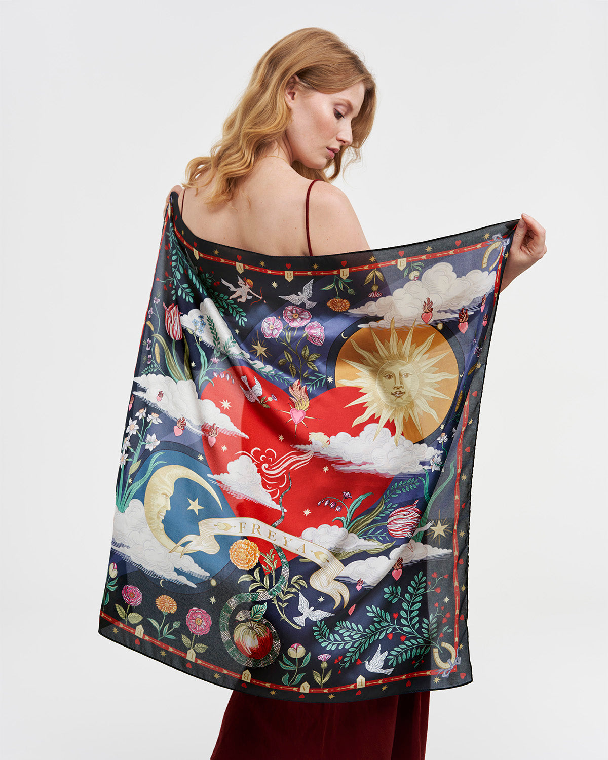 Woman holding a colorful scarf with celestial design on a plain background