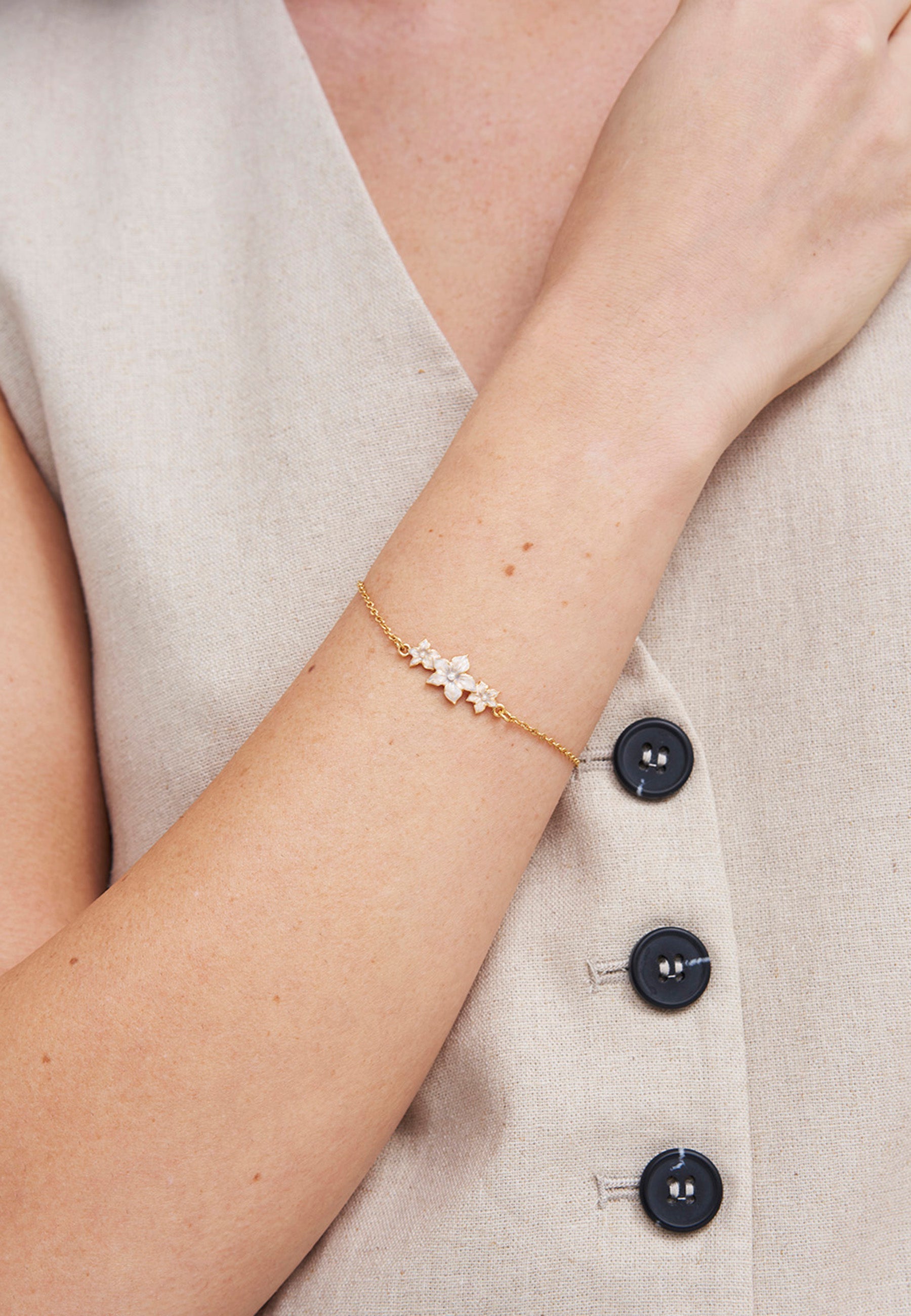 Gold Jasmine & Pearl Bracelet on a wrist against a beige background
