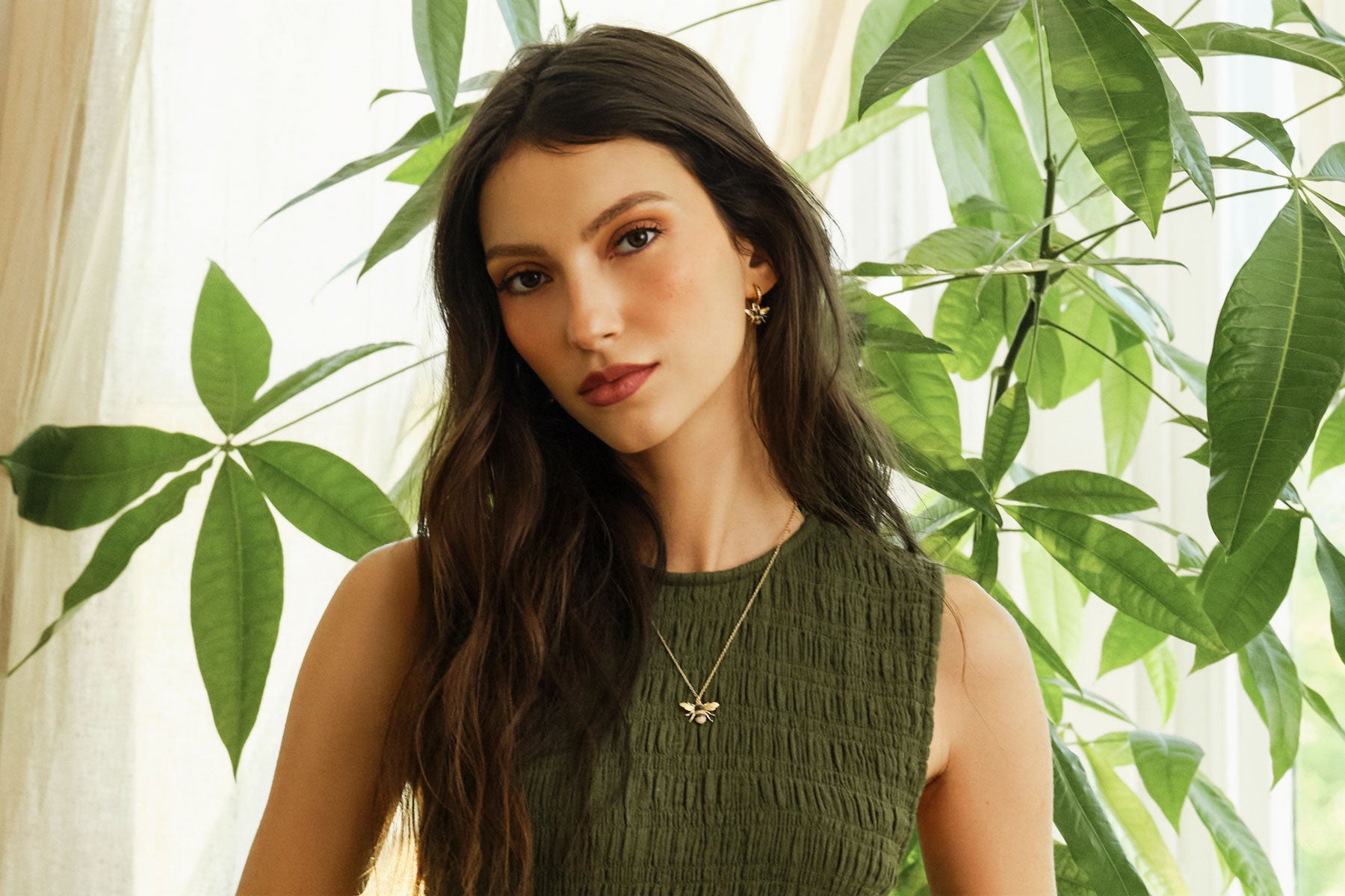 Woman wearing a green dress with a Bee necklace and bee earrings in front of green leaves