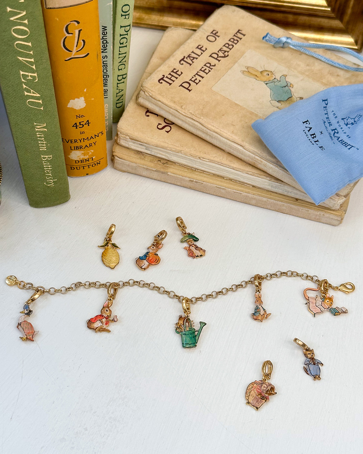 Collection of vintage-style Peter Rabbit jewellery charms and books on a white surface