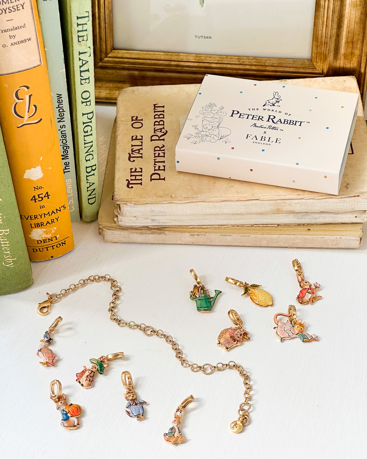gold charm bracelet with gold enamel charm Peter Rabbit characters on a white surface, books in the background