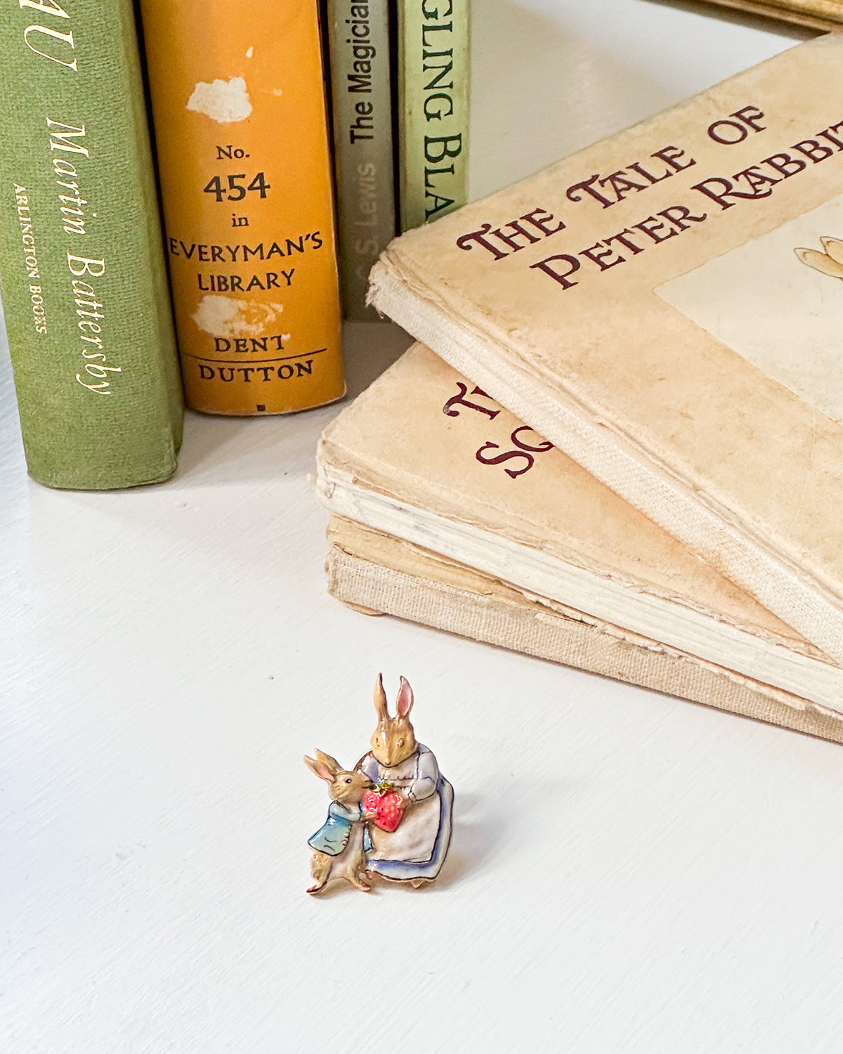 gold enamel brooch of a rabbit holding a strawberry in front of vintage books