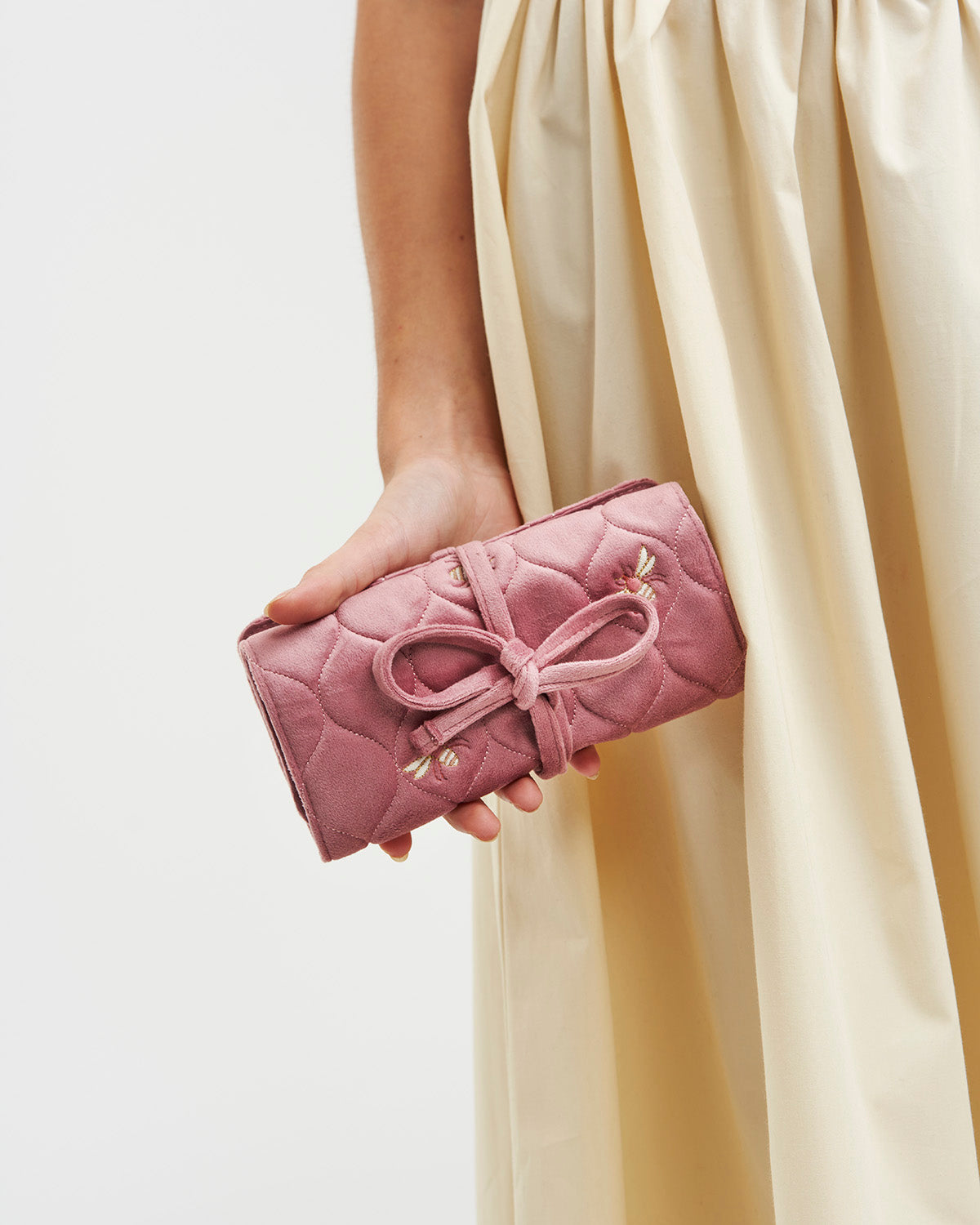Pink quilted clutch with a bow held by a person wearing a beige dress.