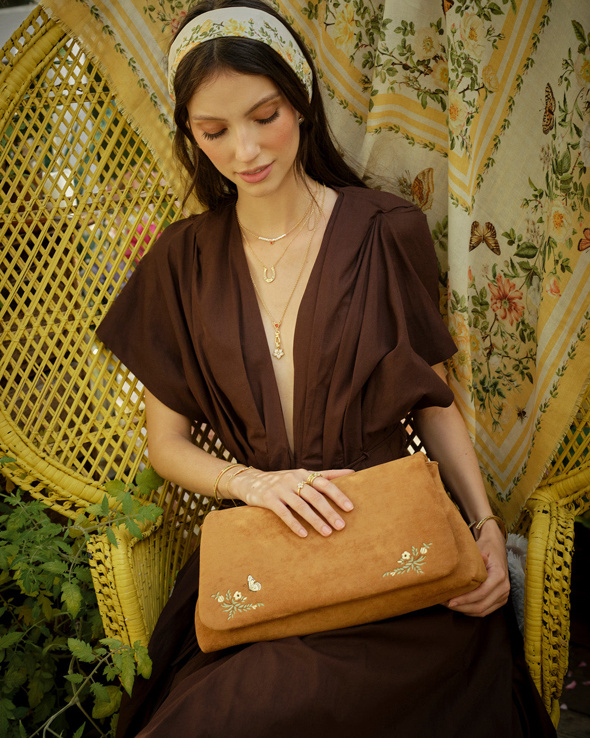 Woman holding a brown clutch in a decorative setting with floral patterns.