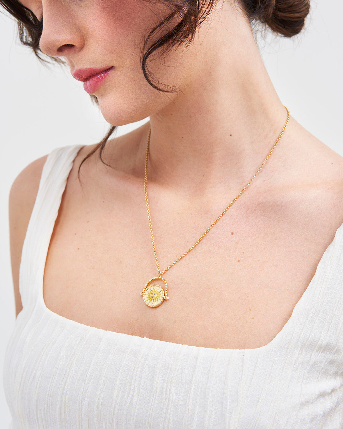 Woman wearing a gold necklace with a white top on a light background