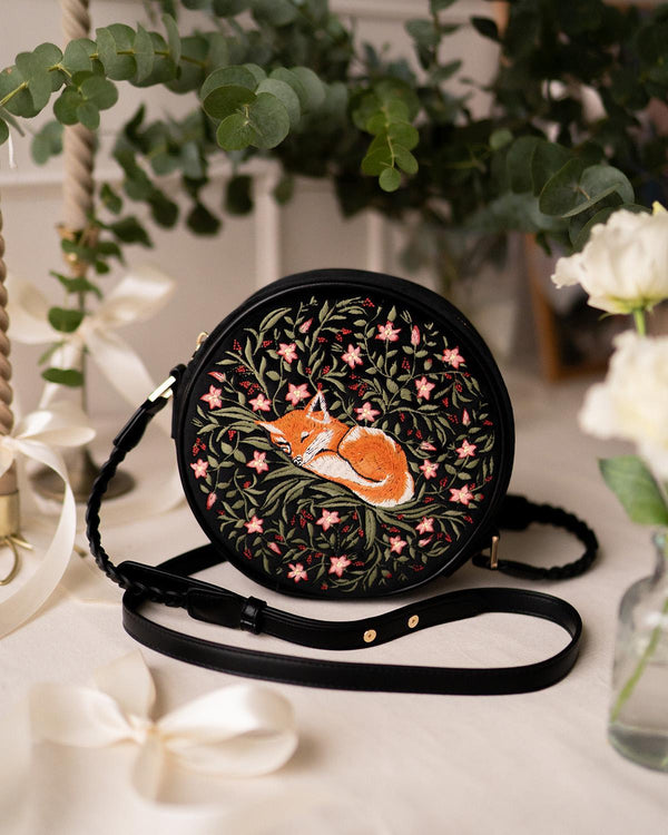 embroidered sleepy fox motif on navy circle crossbody bag on display.