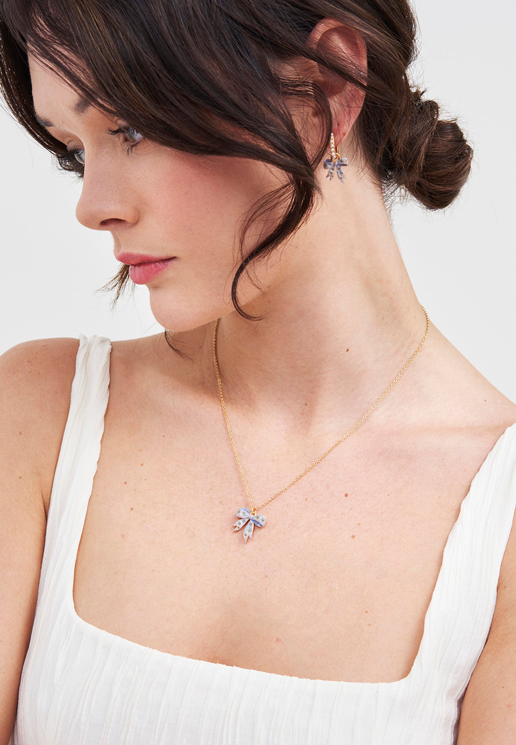 Woman wearing a Gold Forget Me Not Bow Pendant Necklace against a neutral background