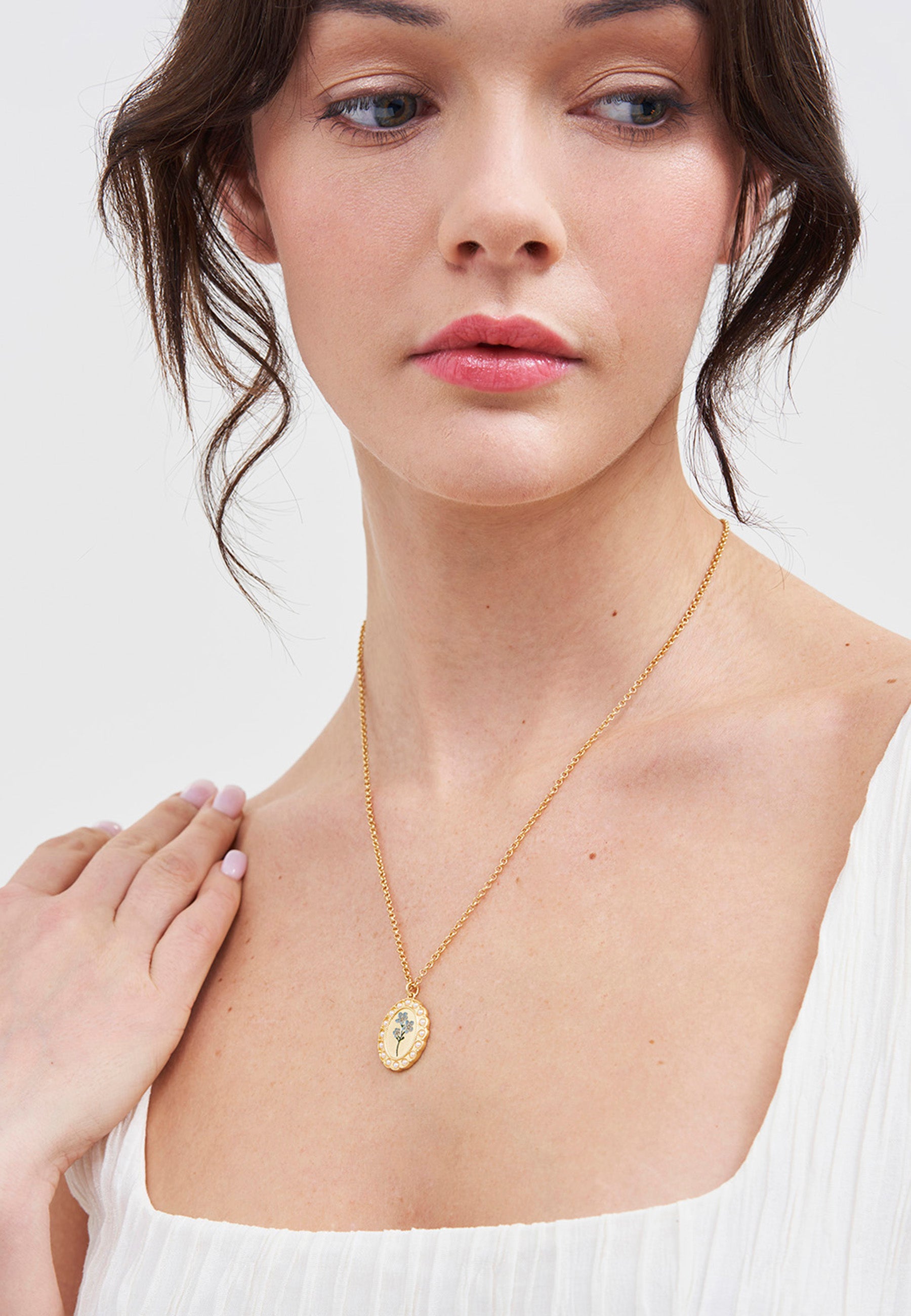 Woman wearing a gold forget me not cameo pearl detail pendant necklace on a plain background