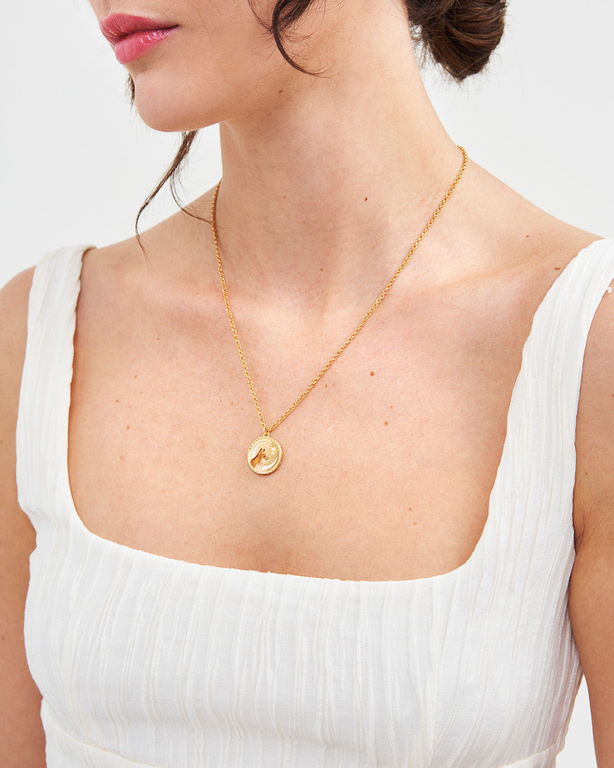 Gold necklace with a pendant worn by a person in a white top on a light background