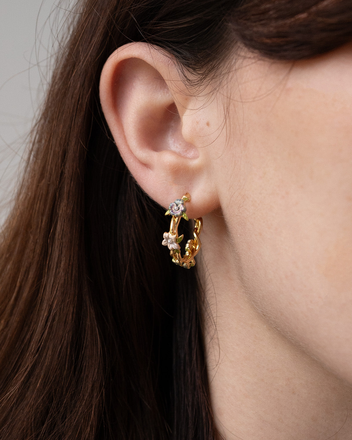 Close-up of a person wearing gold hoop earrings with small enamel flower details.
