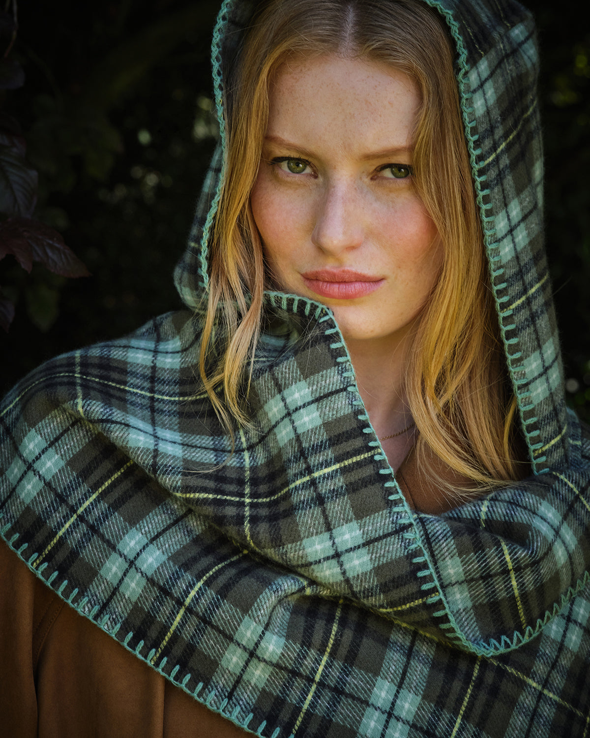 Woman wearing a plaid hooded scarf with a dark background