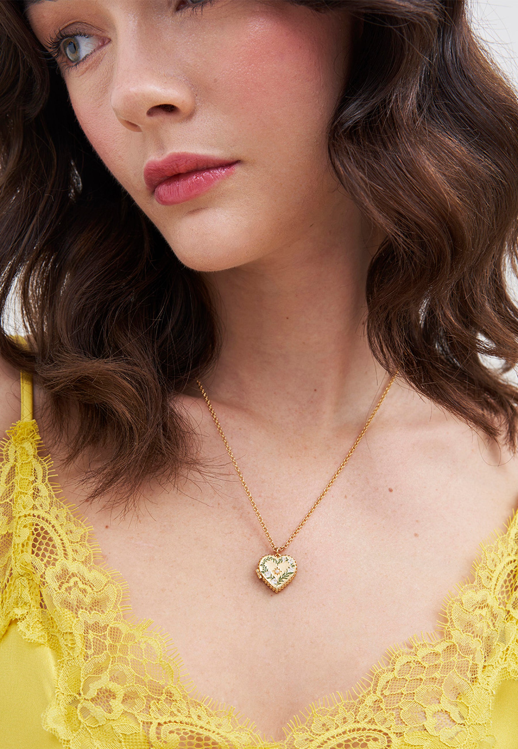 Woman wearing a yellow lace top and a fine gold chain necklace with heart shaped locket pendant.