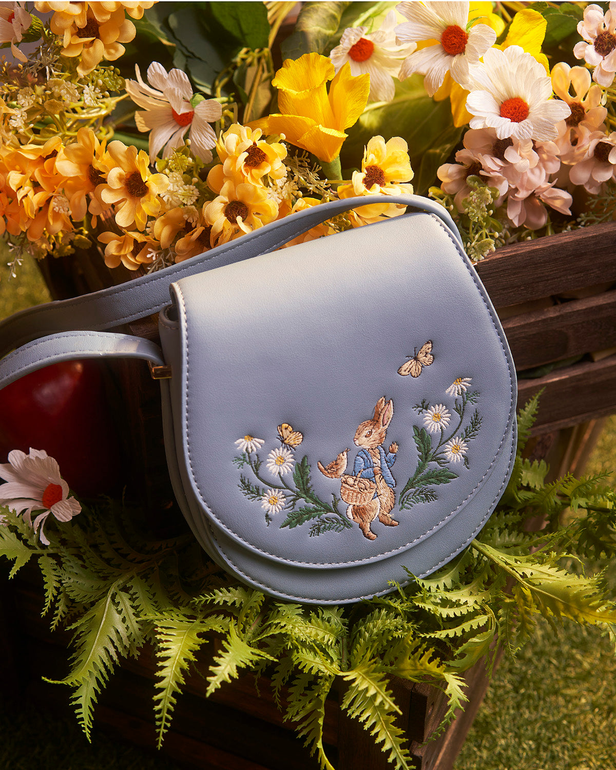 Light blue handbag with embroidery of a rabbit and flowers, surrounded by flowers and plants.