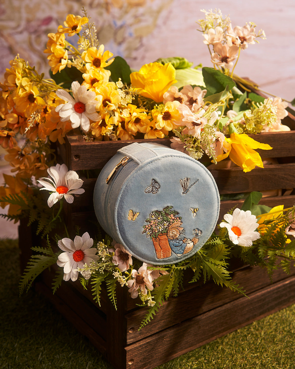 Decorative round box with floral and Peter Rabbit design on a bed of flowers and greenery.